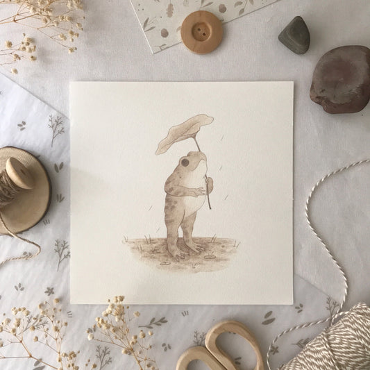 Toad in the Rain Art Print showing a toad under a leaf, perfect for adding nature-inspired charm to any room.